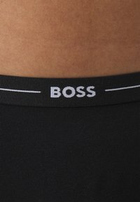 Svart bomullsbelte med "BOSS"-logo i hvite bokstaver, med elastisk tekstur og ribbet mønster.