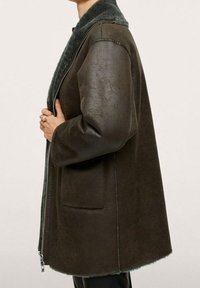 Bruine neplederen jas met een zachte grijze kraag, ritssluiting en twee zijzakken. Gepersonaliseerde pasvorm met een iets uitlopende zoom.