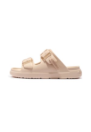 Sandalia beige con dos correas ajustables con hebillas y una suela plana con ranuras. El nombre de la marca está grabado en la correa lateral.