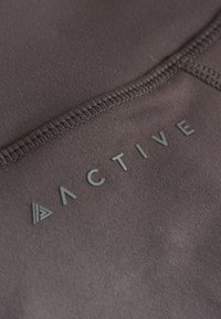 Material textil sportiv negru cu o textură netedă, având cuvântul „ACTIVE” inscripționat gri și un mic logo triunghiular.