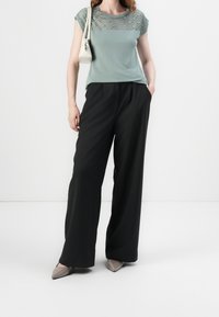 Světle zelený top s texturovanou krajkovou vrstvou, doplněný o černé široké kalhoty s vysokým pasem a špičaté béžové baleríny. Bílá kabelka.