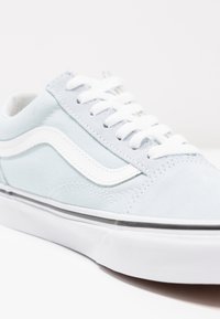 Světle modrý sneaker vyrobený z plátna a semiše, s bílými tkaničkami, bílým bočním pruhem a silnou bílou gumovou podrážkou.