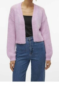 Cardigan rosa lavorato a maglia con un design corto, polsini a coste e apertura frontale, indossato sopra una maglietta nera e abbinato a jeans blu.