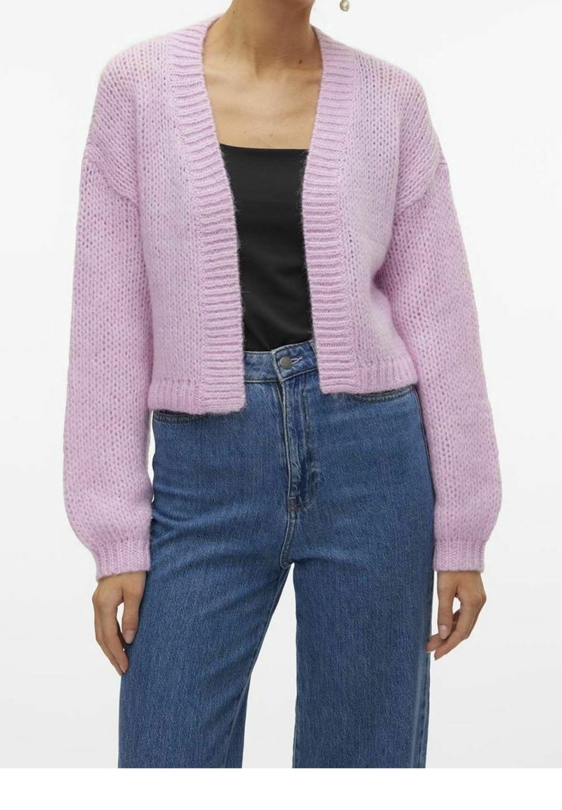Cardigan rosa lavorato a maglia con un design corto, polsini a coste e apertura frontale, indossato sopra una maglietta nera e abbinato a jeans blu.