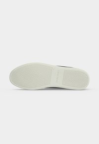 Semelle de chaussure avec une prise en caoutchouc blanche présentant un motif quadrillé et le nom de la marque "Jack & Jones" embossé au centre.