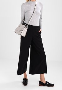 Harmaa pitkähihainen paita, leveät mustat housut, mustat kengät tekstuur yksityiskohdilla ja vaaleanharmaa olkalaukku korostuksilla.