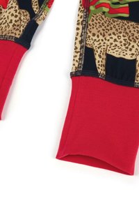 La camisa de manga larga presenta un puño de canalé rojo, con un estampado de leopardo sobre un tejido negro, acentuado por detalles florales y de temática navideña.
