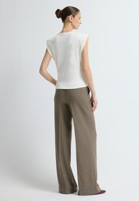 Jasna kremowa bezrękawnikowa bluzka ze strukturalnymi ramionami w połączeniu z brązowymi spodniami w kratę o szerokich nogawkach i burgundowymi czółenkami. Gładka faktura.