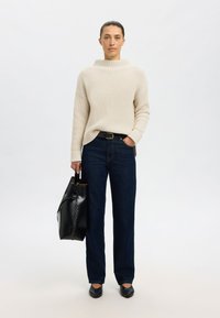 Pull en maille côtelée crème, jean taille haute bleu foncé, sac à main en cuir noir et chaussures plates noires ; design simple et fonctionnel.