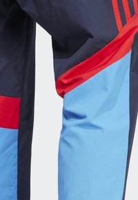 Herren-Sporthose mit einem Farbblockdesign in Marineblau, Rot und Hellblau; aus leichtem, strukturiertem Stoff gefertigt.
