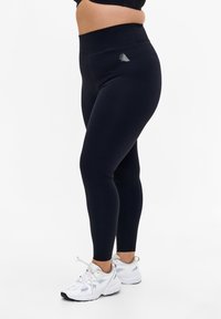 Marine leggings lavet af str�ækbart stof, med en høj talje og et lille logodesign på venstre forside. Kombineret med hvide sportssko.