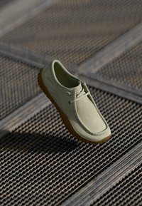 Zapato verde claro con bordes redondeados, hecho de material suave, presenta un diseño sin cordones y una suela flexible de goma marrón.