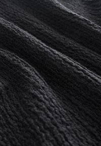 Tissu tricoté gris foncé présentant des motifs côtelés et texturés avec des plis doux et des ombres qui mettent en valeur la profondeur et la structure du matériau.