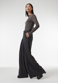 Grijze langärmige fitted top gecombineerd met hoge taille wijde zwarte broek, met zakken en een gladde afwerking. Zwarte plateau schoenen.