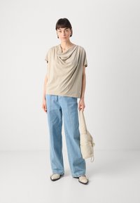 Beige zavěšený top s krátkými rukávy, kombinovaný s volnými modrými džíny a krémovou taškou. Minimalistický design, hladká textura látky.