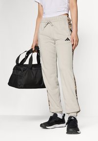 Lys grå joggebukser med svarte detaljer og dyreprint på sidene, kombinert med svarte treningssko og en svart treningsbag.