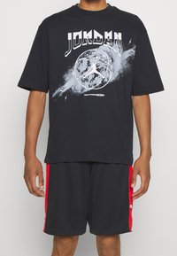 Black cotton t-shirt with short sleeves, featuring white "JORDAN" text and a basketball graphic, paired with black shorts having red side accents.