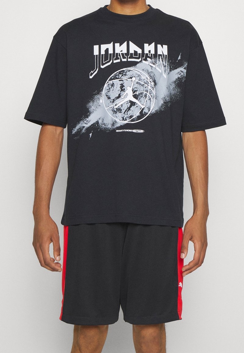 Black cotton t-shirt with short sleeves, featuring white "JORDAN" text and a basketball graphic, paired with black shorts having red side accents.