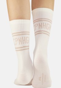 Calze bianche a costine con strisce marroni e il testo "CPNHGN" vicino alla parte superiore. Materiale in misto cotone, aderenti attorno alla caviglia e al polpaccio.