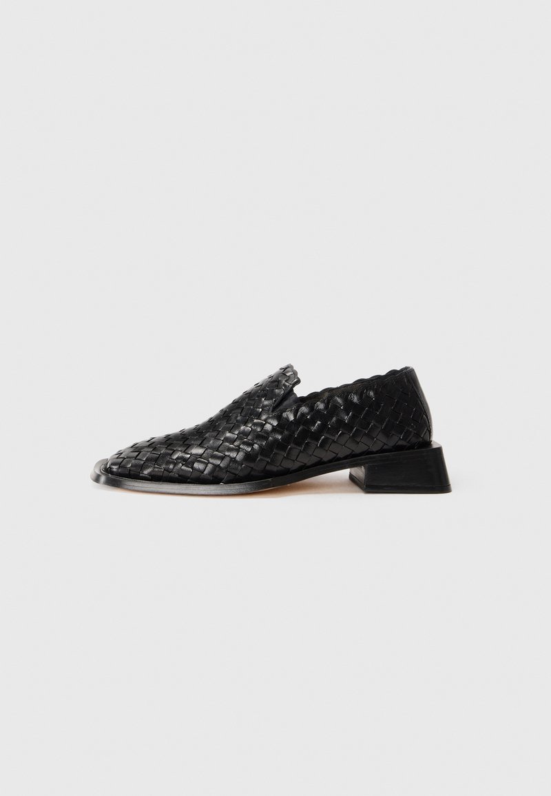 Svart läder vävd slip-on sko med låg klack och scalloped kantdetalj, visad mot en vit bakgrund.