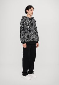 Sweat à capuche noir avec des motifs en texte blanc, doté d'une capuche à cordon de serrage et de poignets côtelés. Associé à un pantalon noir et des baskets blanches.
