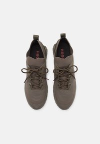 Chaussures de sport marron foncé avec une tige texturée, un bout arrondi et des lacets contrastants. Elles comportent une boucle de maintien et une semelle intérieure avec logo.