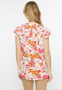 Blusa floreale con sfondo bianco e fiori rosa, arancioni e marroni, maniche puff corte e dettagli arricciati sul colletto.