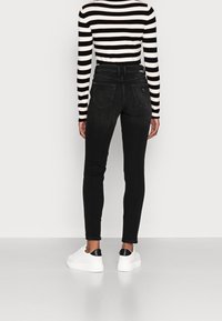 Vaqueros negros de talle alto con un ajuste ceñido, que cuentan con bolsillos traseros y una pequeña etiqueta con el logo. Combinados con una camiseta de manga larga a rayas negras y blancas.