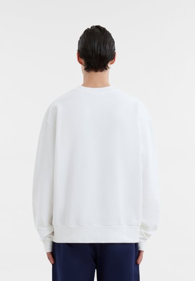 Sweat à col rond blanc, avec épaules tombantes et poignets côtelés ; texture douce ; design simple sans motifs ni accents.