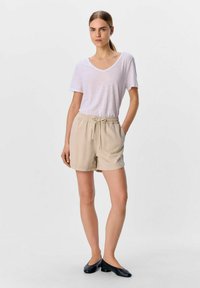 Lys grå V-hals t-shirt parret med beige shorts med elastisk talje. Sorte slip-on sko fuldender outfittet. Simpelt, casual design.