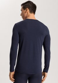 Marineblauw shirt met lange mouwen, gemaakt van zachte, lichte stof. Het heeft een ronde halslijn en aansluitende mouwen, met een gladde, gelijkmatige textuur.