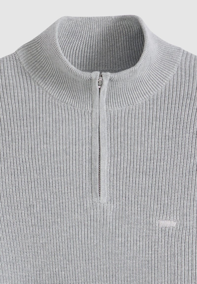 Pull gris clair à fermeture éclair quart de tour avec une texture côtelée, doté d'une fermeture éclair métallique et d'un petit logo brodé à l'ourlet.