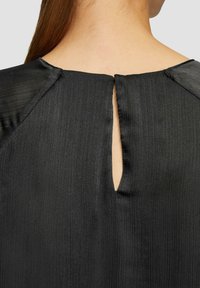Zwarte jurk van een geweven, geribbelde stof. Heeft een keyhole-opening aan de achterkant en een subtiele glans. Strak model met elegante ontwerpelementen.