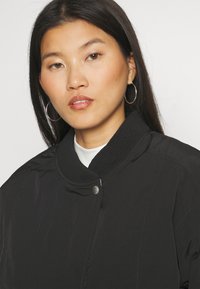 Black bomber jacket with a ribbed collar, snap closure, and smooth texture. Features a minimal design and subtle sheen.