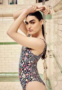 Cvečni enodelni kopalke z črnim ozadjem, ki prikazuje različne barvite cvetje. Eleganten dizajn z širokimi naramnicami in odprtim hrbtom.