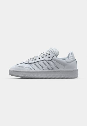 White leather sneaker with a rounded toe, three stripes design on the side, and textured rubber sole. Features round laces and a cushioned collar.