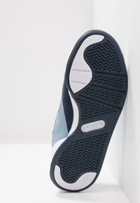 Sneaker Lacoste avec une semelle en caoutchouc, tige en cuir et daim bleu foncé, accents blancs, motif de semelle en zigzag et détail de logo embossé.