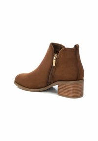 Stivale alla caviglia in suede marrone con punta arrotondata, cerniera laterale e tacco impilato. Il design presenta una texture liscia e una silhouette pulita.