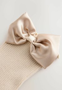 Beige Stricksocken mit einer großen, glatten Satin-Schleife in ähnlichem Farbton an der Spitze. Der Stoff hat eine gerippte Textur.