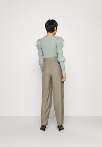 Mentolově zelený, texturovaný top s nabíranými rukávy a přiléhavým střihem, spárovaný s béžovými kalhotami s vysokým pasem a širokými nohavicemi a černou špičatou obuví.