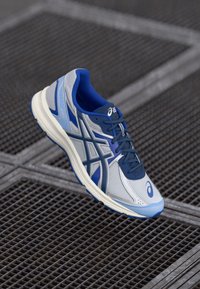 Hallitusjalatsid, millel on hallist ja sinisest võrgust ülemine osa, iseloomustavad pehmendusega tallad, kontrastsed aktsendid ning nööpidega disain.