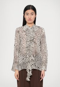 Bluza crem transparentă cu un model cu pete maro și negre. Are un volan în partea din față, mâneci lungi și un guler înalt.