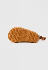 Semelle de chaussure en caoutchouc avec un motif texturé en nid d'abeille de couleur brun clair; présente un onglet surélevé avec un accent marron.