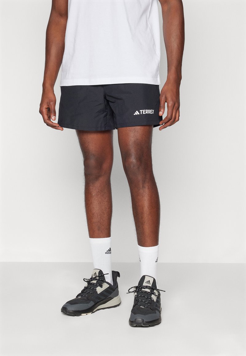 Shorts de sport noirs avec une taille élastique et le logo blanc "TERREX". Portés avec des chaussettes blanches et des baskets noires avec des accents gris.