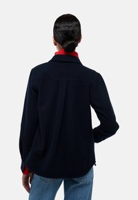 Veste chemise en mélange de laine bleu marine, avec un col côtelé rouge, des manches longues et un ourlet légèrement incurvé, conçue pour une coupe décontractée.