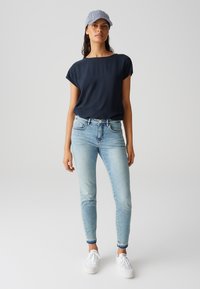 Top navy a maniche corte, jeans skinny azzurri chiari e sneakers bianche. I jeans hanno un orlo sfilacciato; il cappello è a righe. Outfit semplice e casual.