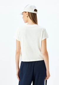 Witte, cropped katoenen T-shirt met korte mouwen, gezien vanaf de achterkant, gecombineerd met marineblauwe broek, met een relaxte pasvorm en eenvoudig ontwerp.