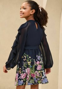 Rochie bleumarin cu mâneci lungi volănașe, imprimeu floral la tiv și detaliu cu decupaj la spate. Material neted cu talie măsurată.