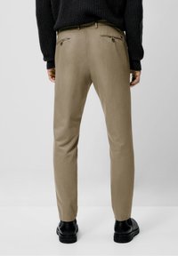 Beige, slim-fit broeken met een gladde textuur, voorzien van twee achterzakken met ritssluiting, gecombineerd met zwarte enkellaarsjes.
