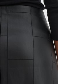 Gonna nera in pelle con un design strutturato, caratterizzata da pannelli rettangolari e dettagli di cucitura prominenti, che mette in mostra una texture liscia.